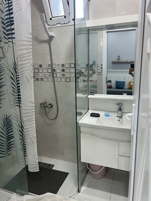 Un baño con cabina de ducha de vidrio, lavabo con espejo e inodoro.