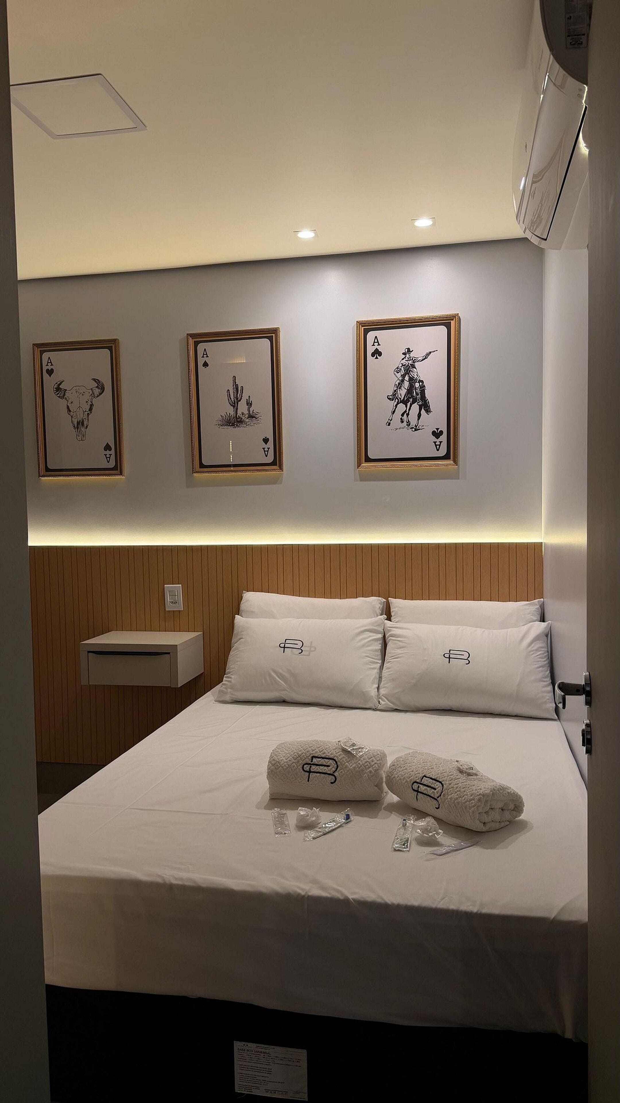 A hotel room with a bed, pillows, a nightstand, and wall art.