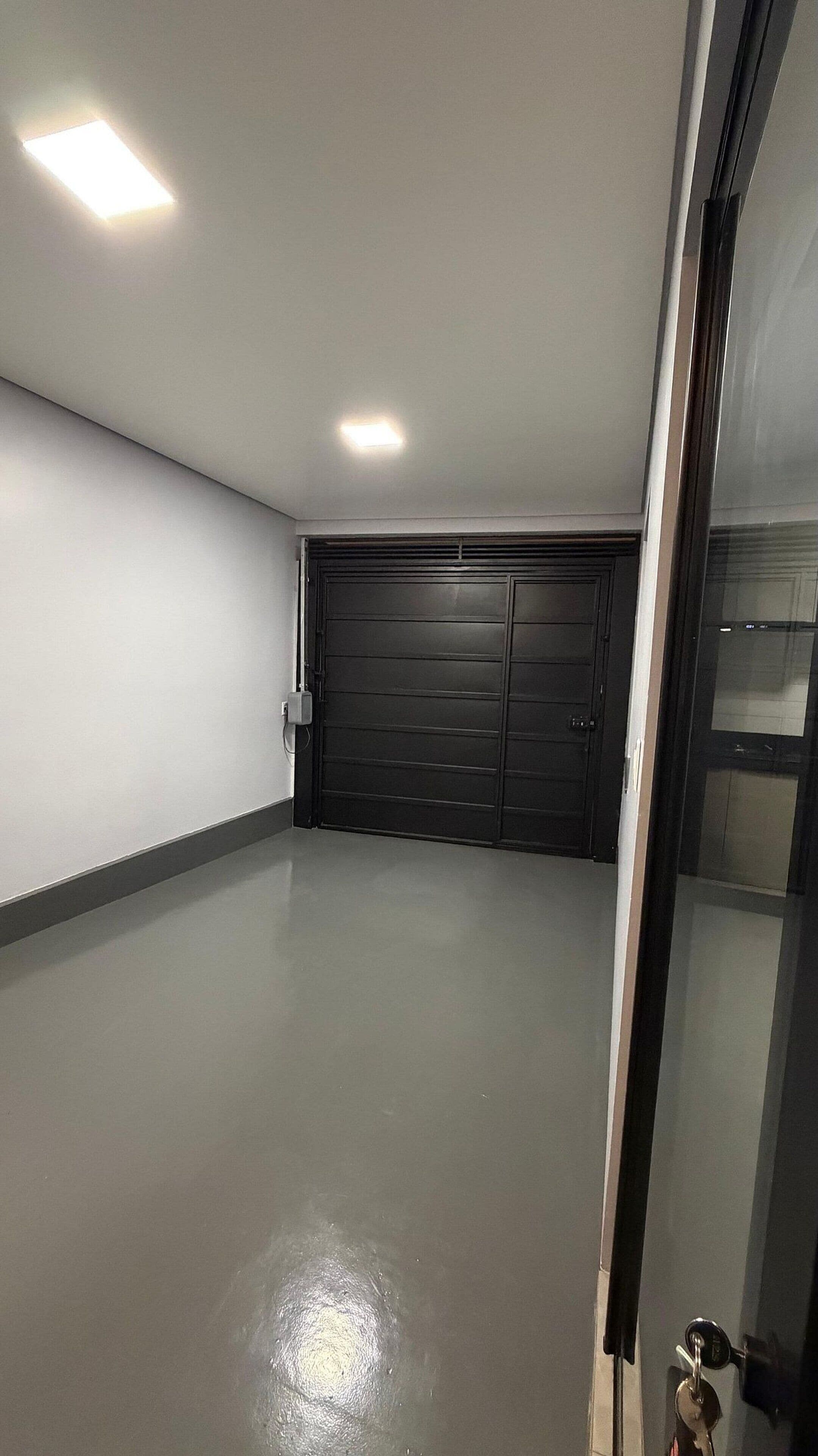 Uma garagem limpa e vazia, com uma porta escura e uma luminária no teto.