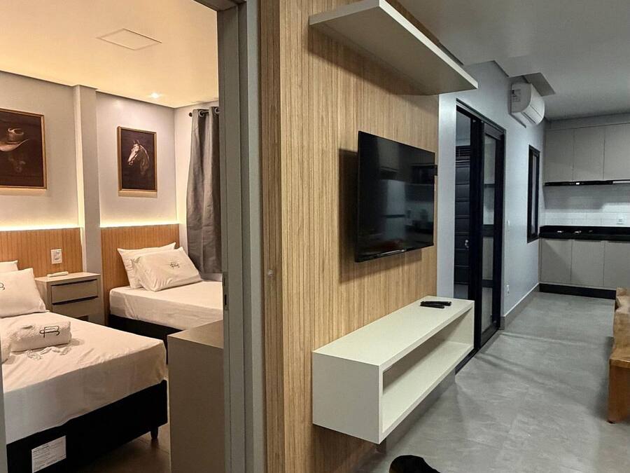 A modern hotel room with a flat-screen TV mounted on a wooden panel, a sofa, and a dining area with a table and chairs.