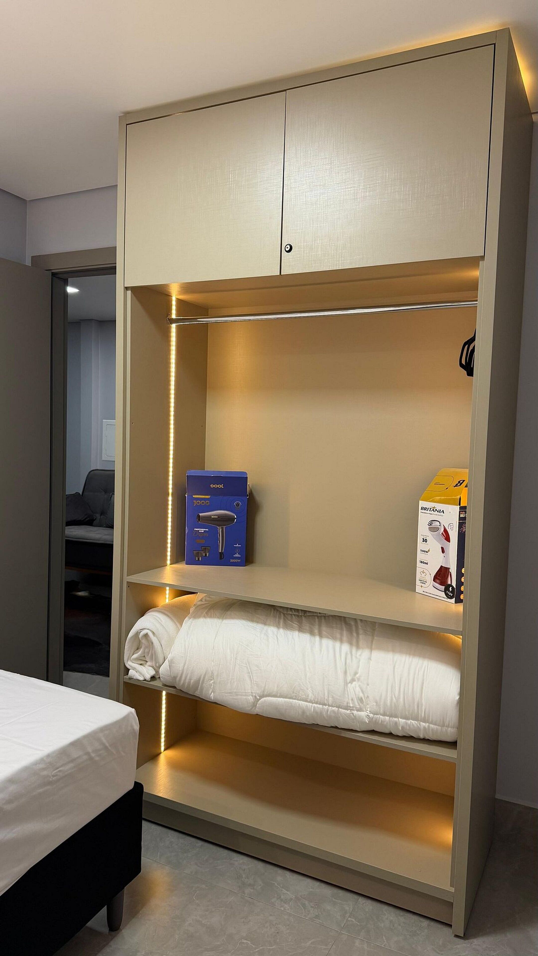 A compact bed with a storage cabinet above it, a box of toiletries, and a bedside table.