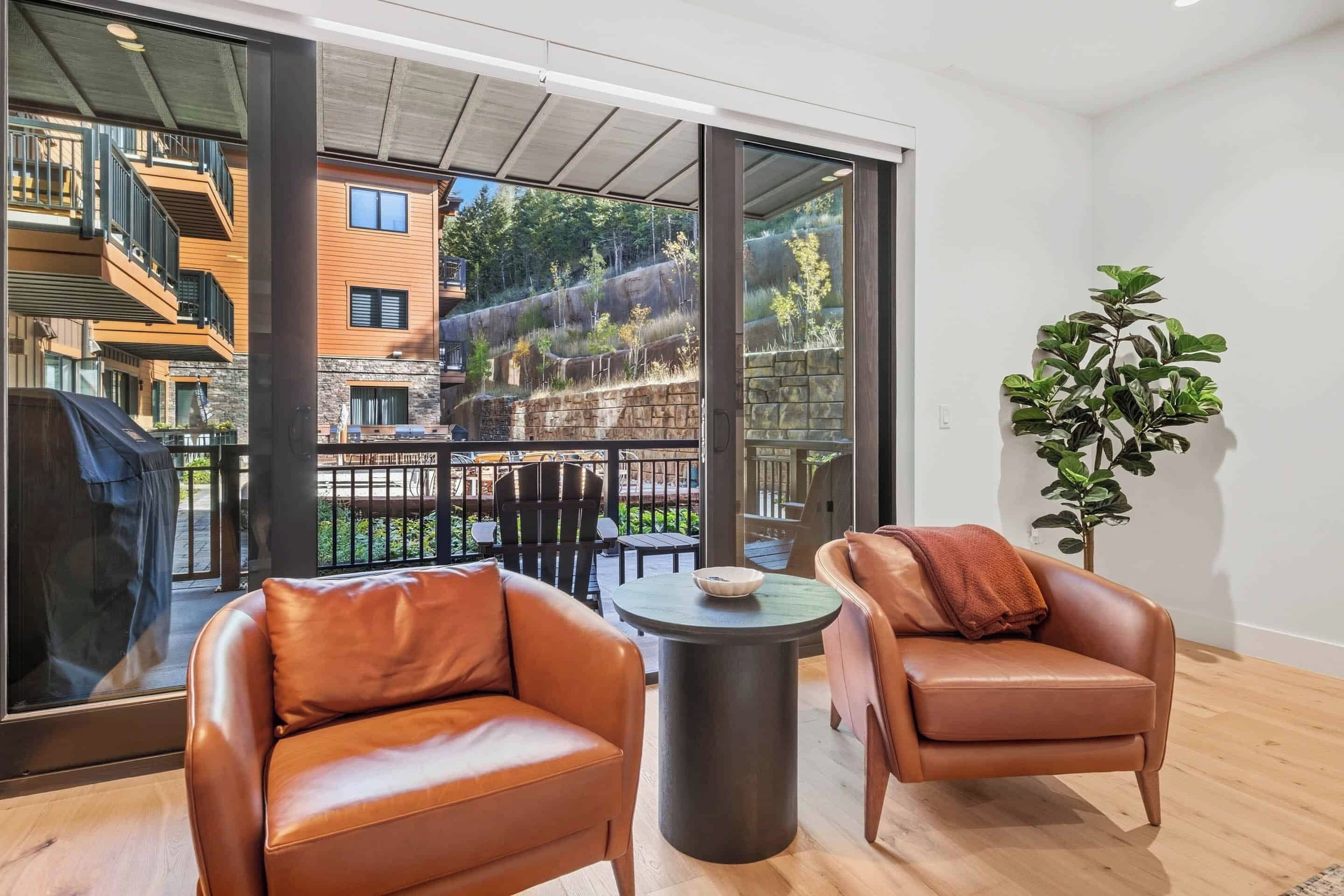 Un appartement moderne doté d’un balcon, de fauteuils en cuir, d’une petite table ronde et d’une plante en pot.