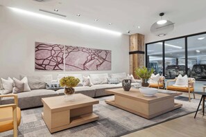 Ein modernes Wohnzimmer mit einem grauen Sofa, zwei Holztischen und einem großen abstrakten Gemälde an der Wand.