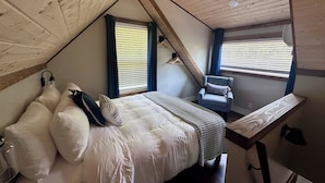 Une chambre avec un plafond en pente, un lit avec une literie blanche, une chaise et un bureau.