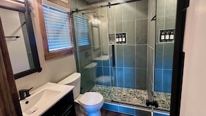 Une salle de bain avec une douche à parois de verre, des toilettes blanches, un lavabo et un miroir.
