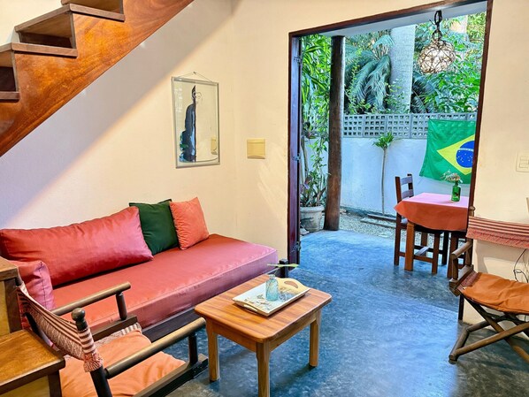 A room with a red sofa, wooden table, and chairs, a staircase, and a view of greenery outside. - Oceana Suites Veralucia (Tibau do Sul)