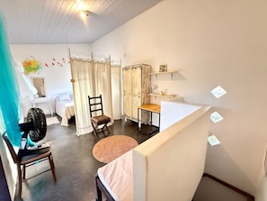 Une pièce comprenant un lit, une chaise, une table, un ventilateur et un rideau.