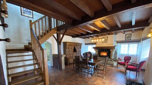 Amplia sala de estar con escalera de madera, chimenea y comedor con sillas y mesa.
