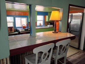 A kitchen with a refrigerator, stove, and chairs.