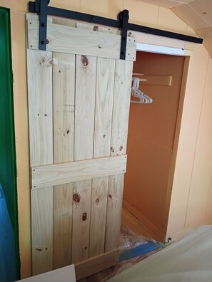 Une porte coulissante en bois, dotée d’un rail en métal noir, d’un cadre de porte vert et d’une feuille de plastique sur le sol.