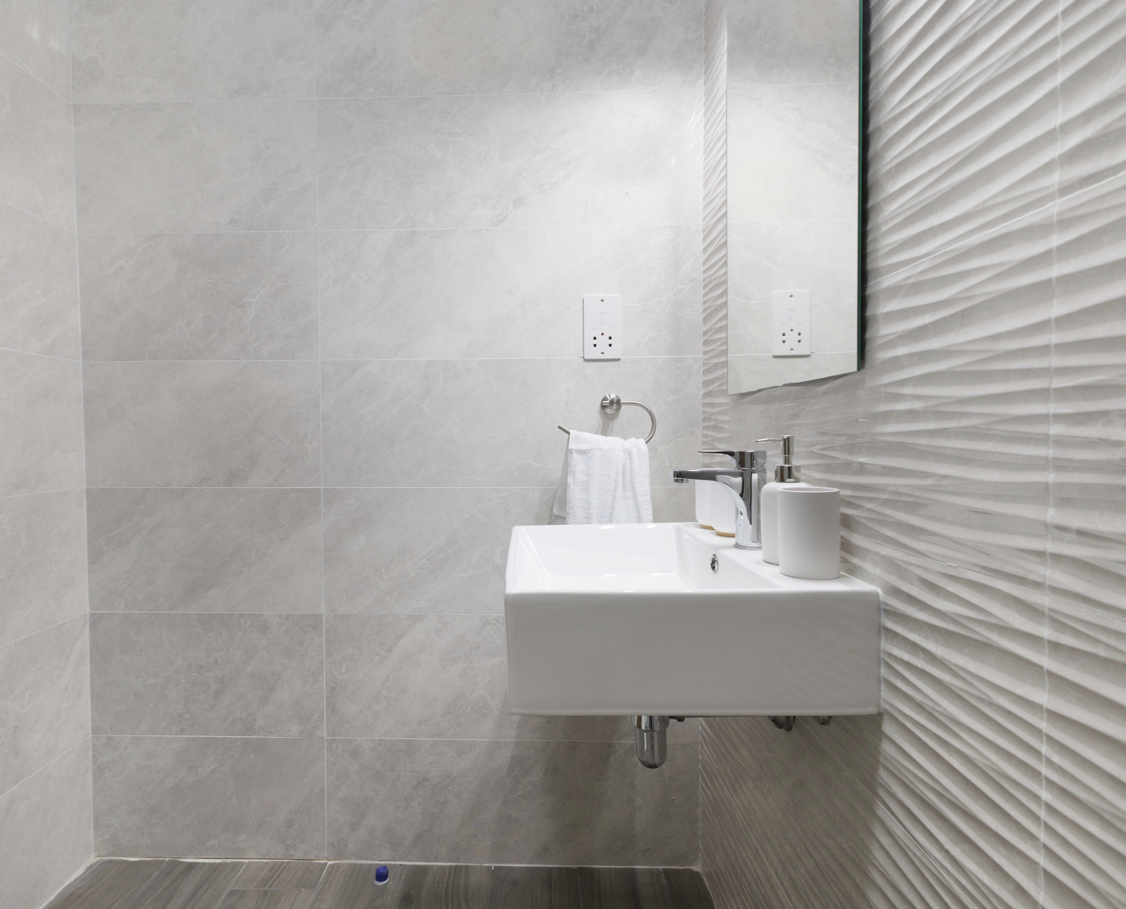 Un baño moderno con un lavamanos blanco, toallero y espejo con pared texturizada.