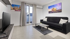 A modern living room with a flat-screen TV, a black sofa, a coffee table, and two paintings on the walls. - Spacious 2BR Podium Marina near Valletta (Msida)