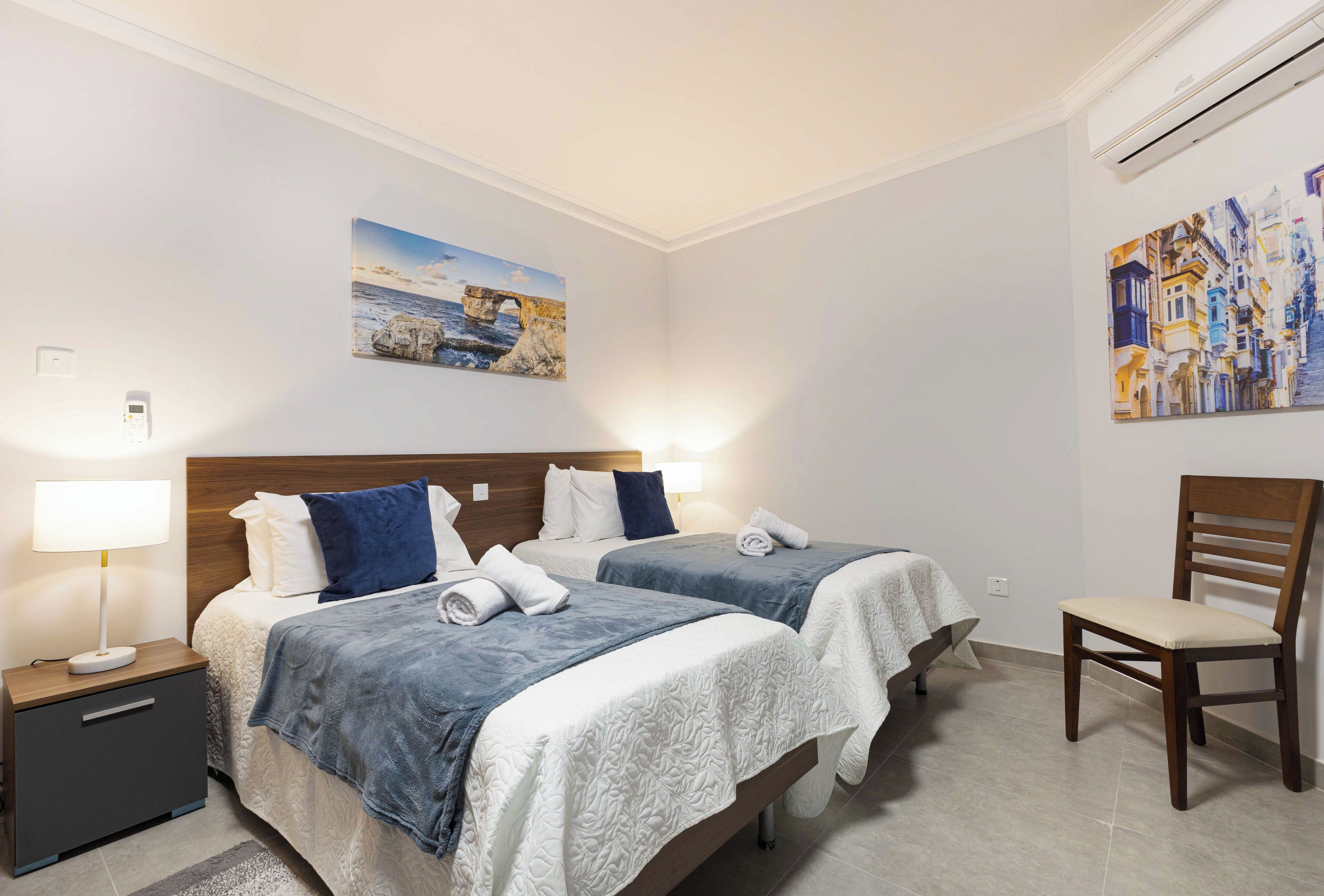 A hotel room with two beds, a nightstand, a chair, and artwork on the walls.