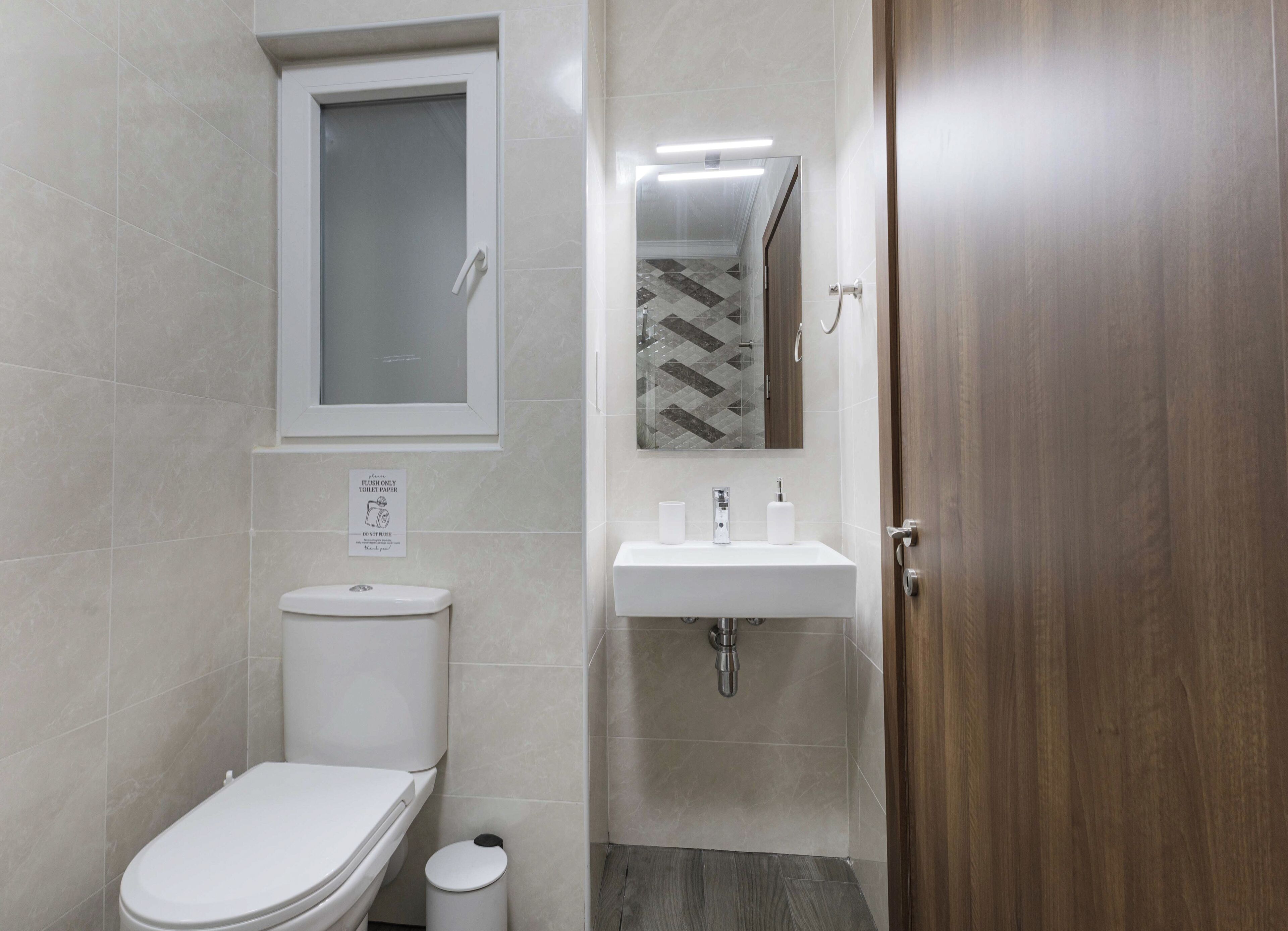 A bathroom with a toilet, sink, mirror, and a door.