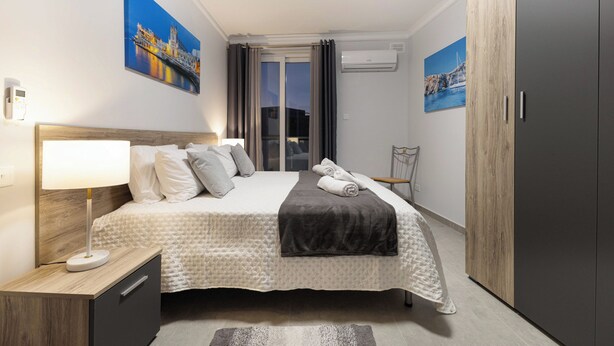 A neatly arranged hotel room with a bed, bedside lamp, and artwork on the walls. - Spacious 2BR Podium Marina near Valletta (Msida)