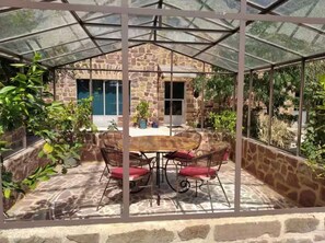 Une terrasse couverte avec un mur en pierre, une table avec des chaises et des plantes en pot.