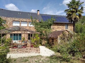 Une maison en pierre avec un patio, des panneaux solaires et un palmier.