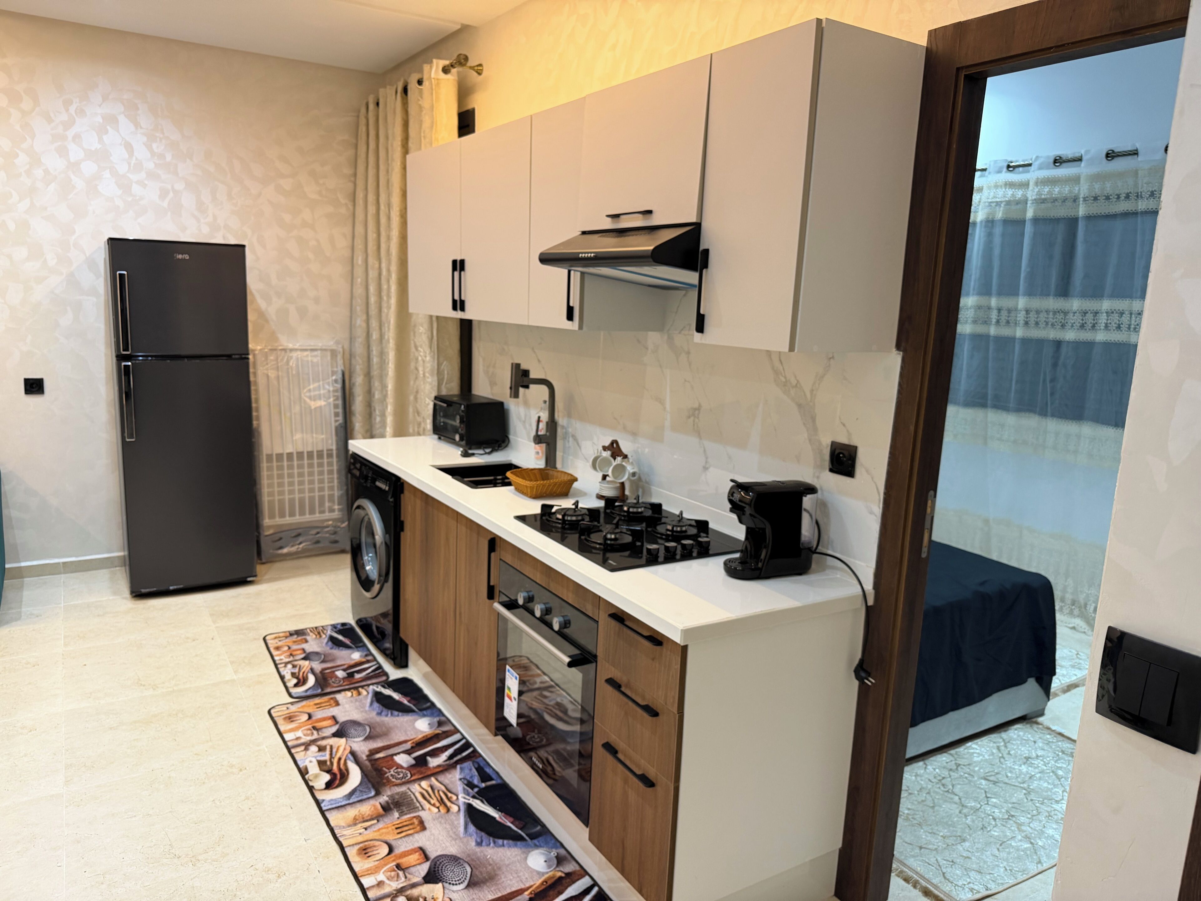 A compact kitchen with a refrigerator, washing machine, stove, and coffee maker.