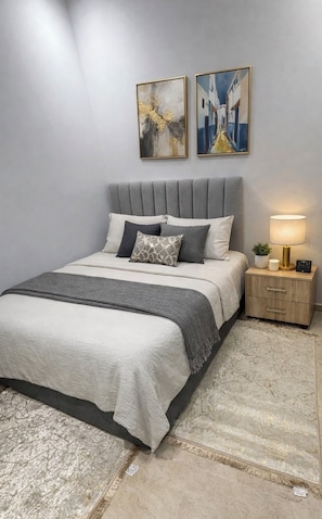 A bedroom with a bed, a nightstand, a lamp, and two paintings on the wall. - Steps to the Beach. NEW 1BR with Garage & Netflix (Kenitra)