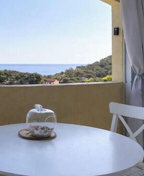 A round table with a teapot and saucer, a white chair, and a view of the sea and greenery. - Apartment, terrace sea view in Saint-Raphaël (Saint-Raphaël)