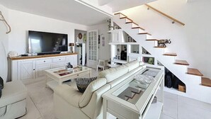 Ett modernt vardagsrum med en stor platt-TV, en soffa, ett soffbord och en trappa med trästeg.