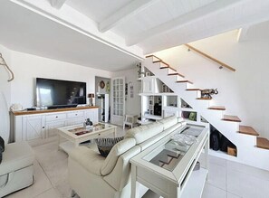 A modern living room with a large flat-screen TV, a sofa, a coffee table, and a staircase with wooden steps. - Apartment, terrace sea view in Saint-Raphaël (Saint-Raphaël)