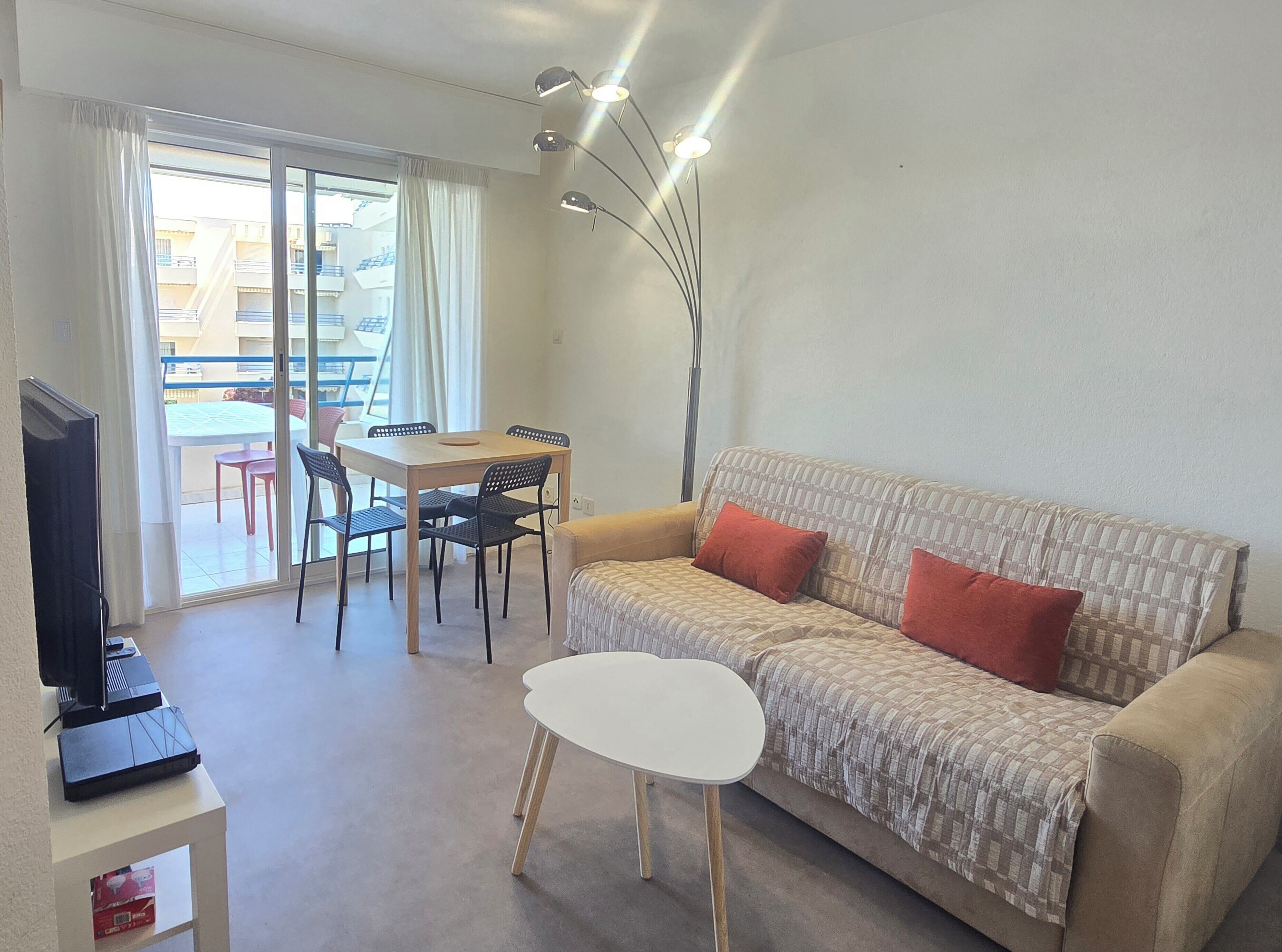 A living room with a sofa, a small table, a TV, and a dining area with chairs and a table.