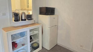 Eine kompakte Küchenzeile mit einem weißen Kühlschrank, einer Mikrowelle, einem Toaster und einem Schrank mit Glastüren, der Geschirr und Gläser beherbergt.