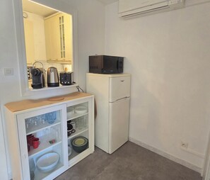 A compact kitchenette with a white refrigerator, a microwave, a toaster, and a cabinet with glass doors containing dishes and glasses. - Studio for 4 with pool, 350m from beach (Fréjus)