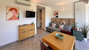 En moderne stue med sofa, fjernsyn, et træbord med skål og et spiseområde.