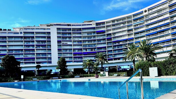 Et moderne hotel med en stor swimmingpool, flere balkoner og palmer.