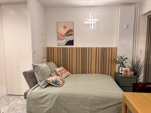 Ein Schlafzimmer mit einem Bett, einem Holz-Kopfteil, einer Wandleuchte, einem gerahmten Kunstwerk und einem Nachttisch mit einer Pflanze.