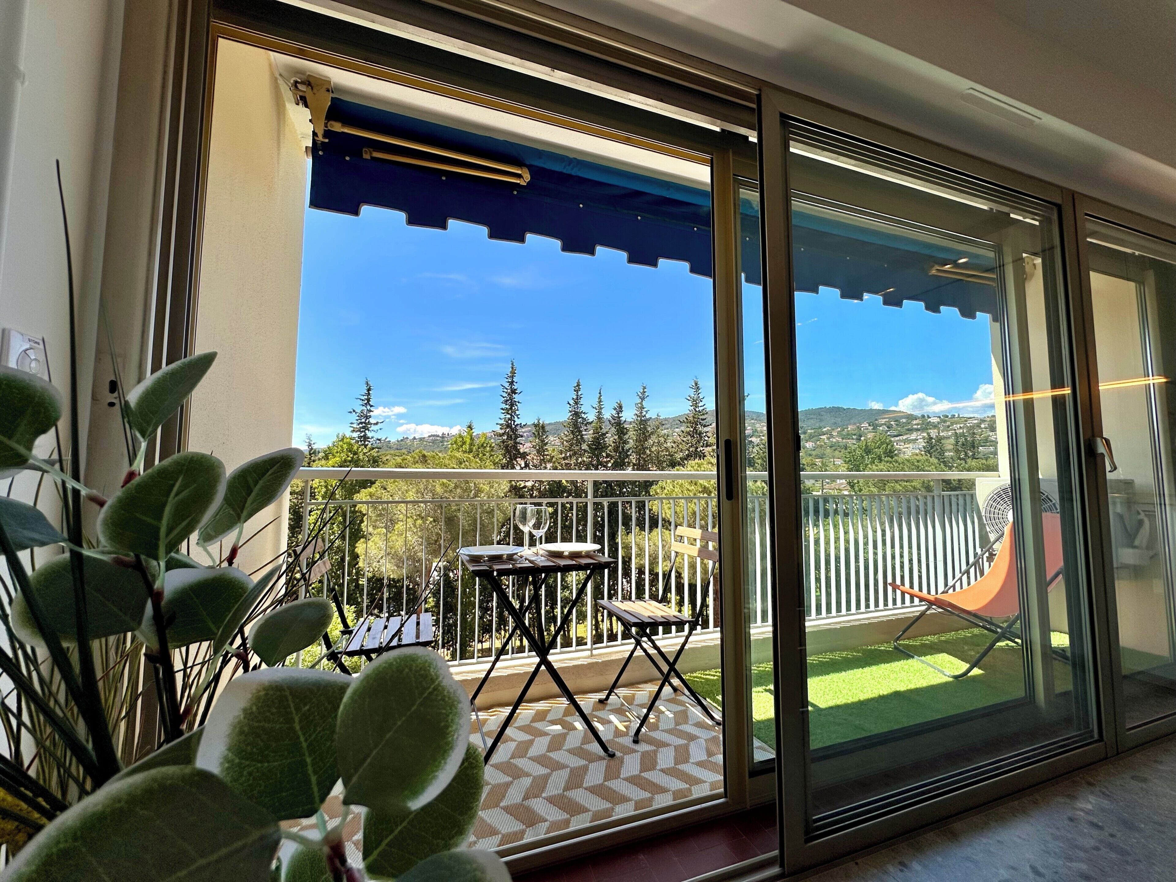 A balcony with a table and chairs, a fan, and a view of a green landscape.