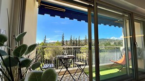 En balkon med bord og stole, en ventilator og udsigt over et grønt landskab.