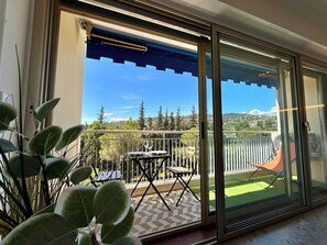 Ein Balkon mit Tisch und Stühlen, einem Ventilator und Blick auf eine grüne Landschaft.