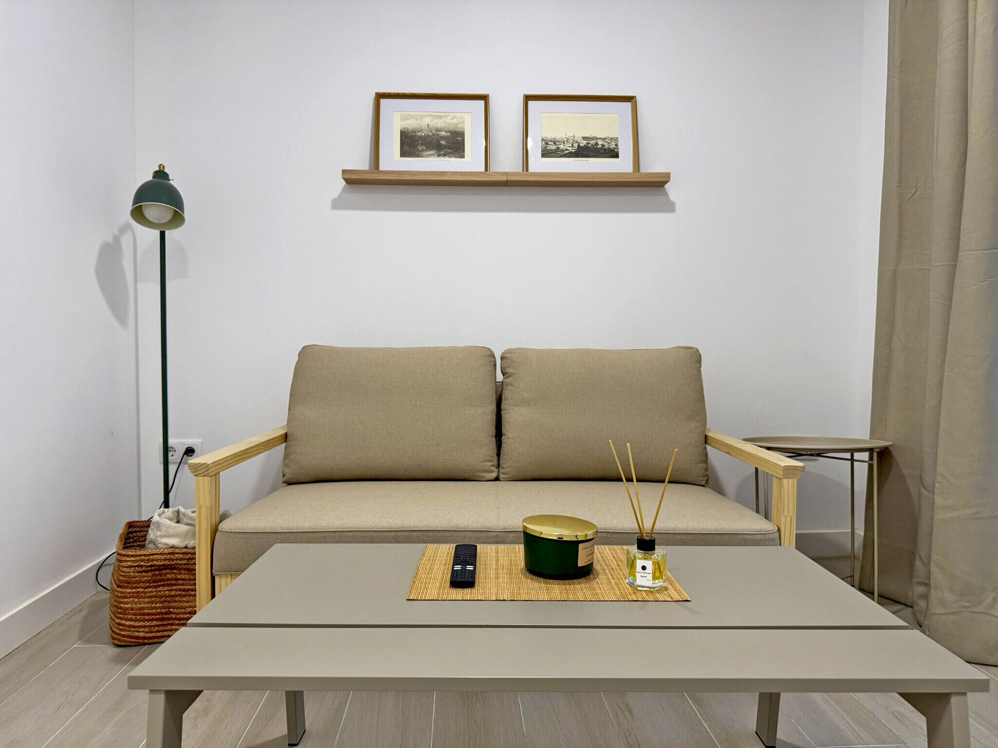 A minimalist living room with a sofa, a coffee table, a lamp, and two framed pictures on the wall.