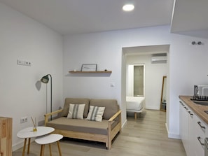 A modern, minimalist living space with a sofa, a small table, a lamp, and a kitchen area. - La Casa de Juana I - Ole Solutions (Jerez de la Frontera)