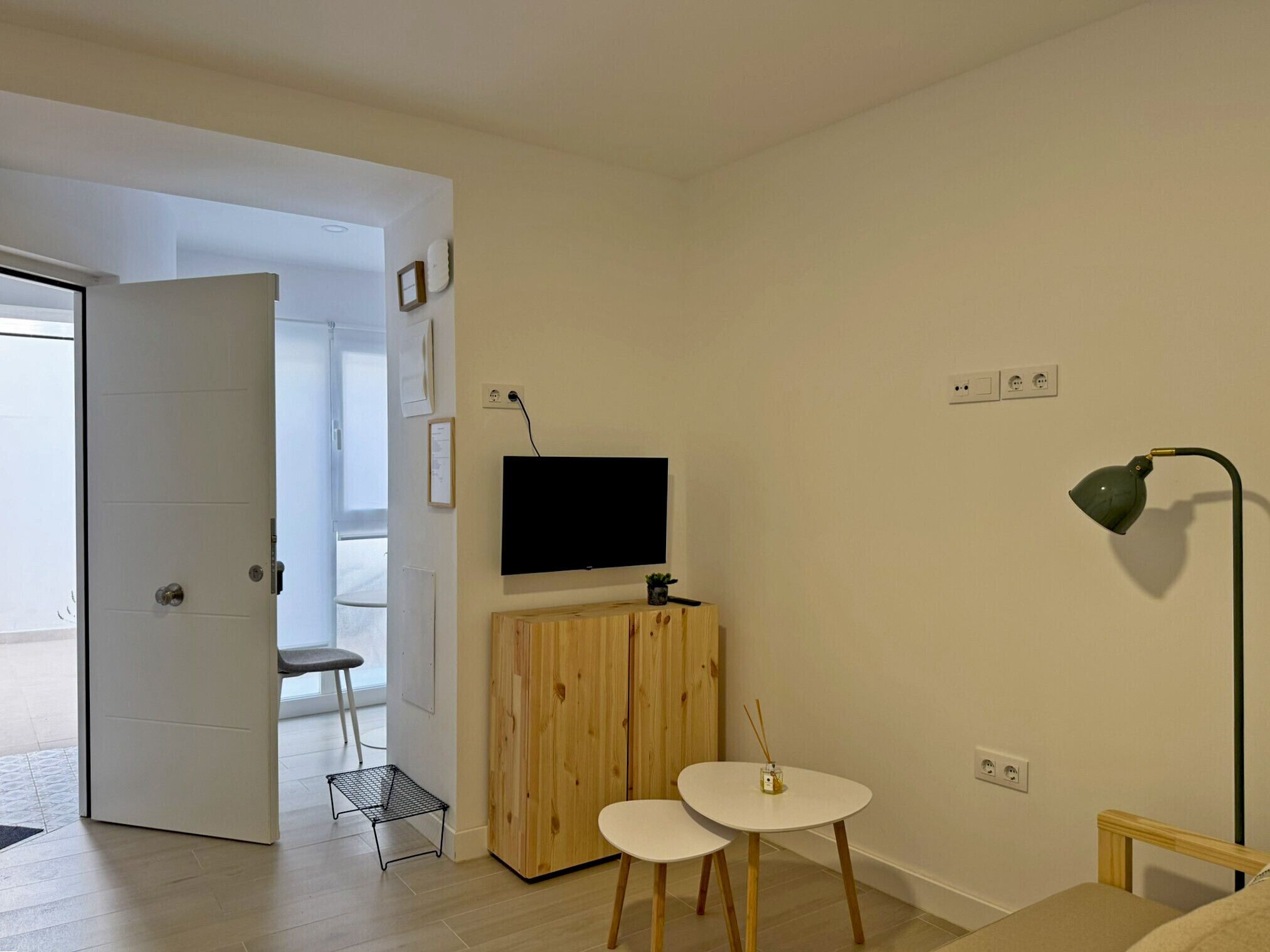 Habitació amb televisió, taula petita, cadira, làmpada i porta que dona a una altra habitació.