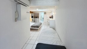 Ein schmaler Raum mit einem Bett, einer kleinen Küchenzeile und einem durch eine offene Tür einsehbaren Badezimmer.