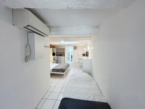 Ein schmaler Raum mit einem Bett, einer kleinen Küchenzeile und einem durch eine offene Tür einsehbaren Badezimmer.