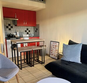 Un espacio habitable compacto con kitchenette, comedor y sofá con cojín.