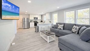 A modern living area with a grey sofa, a coffee table, and a kitchen in the background. - San-Joy Retreat #9, 2BR Condo, Steps to Beach (Myrtle Beach)