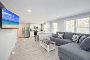 Ein modernes Wohnzimmer mit grauem Sofa, einem Couchtisch und einer Küche im Hintergrund.