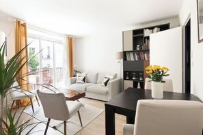 Ein modernes Wohnzimmer mit einer Couch, einem Esstisch, Stühlen, einem Bücherregal und einem Blumentopf.