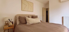 A bedroom with a bed, pillows, a nightstand, a lamp, and a radiator. - Bright apartment with a view in Saint-Raphaël (Saint-Raphaël)