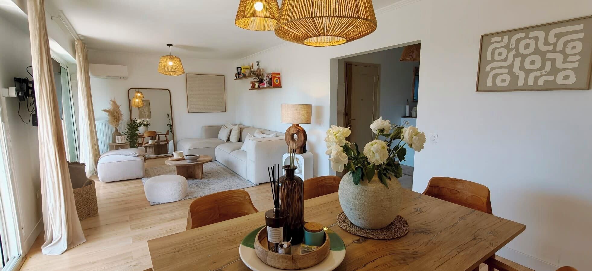 A modern living room with a dining area, featuring a wooden dining table, white sofas, and a large mirror.