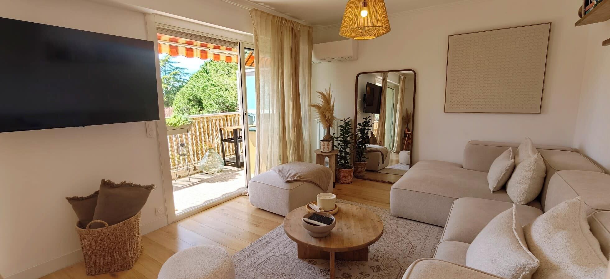 Ein Wohnzimmer mit einer Couch, einem Couchtisch, einem Fernseher und einer Glastür, die zu einem Außenbereich führt.