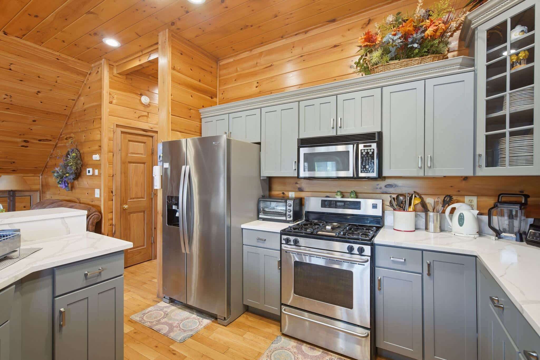 A kitchen with stainless steel appliances, grey cabinets, and a wooden ceiling.