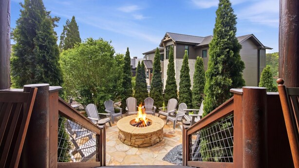 A circular stone fire pit with chairs around it, surrounded by a wooden deck and stone flooring. - Lazy Bear Retreat (Blue Ridge)