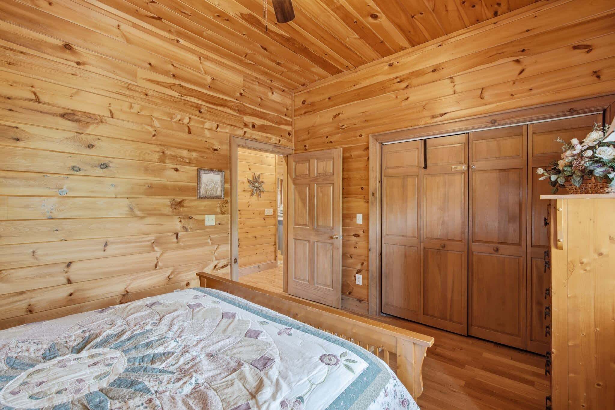 A wooden cabin interior with a bed, a wardrobe, and a door leading to another room.